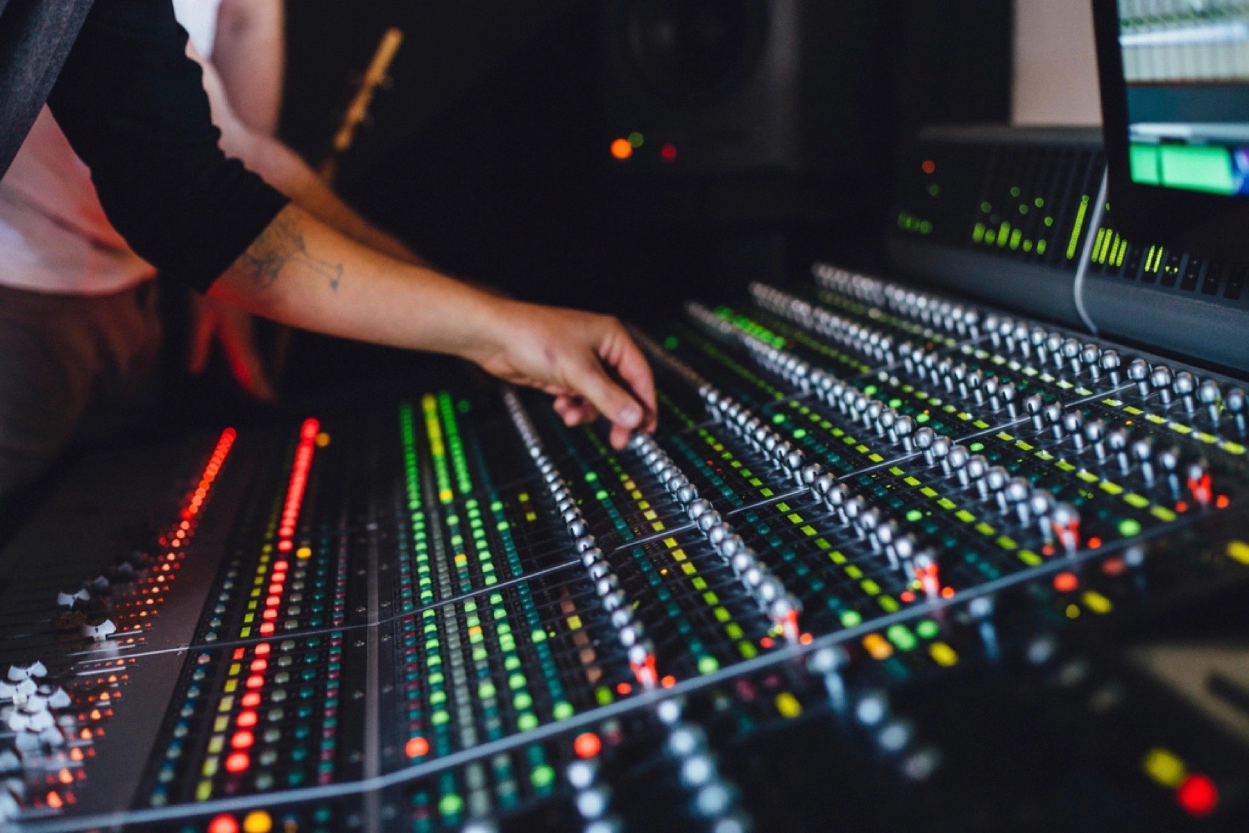 Hands adjusting faders on a studio mixing console